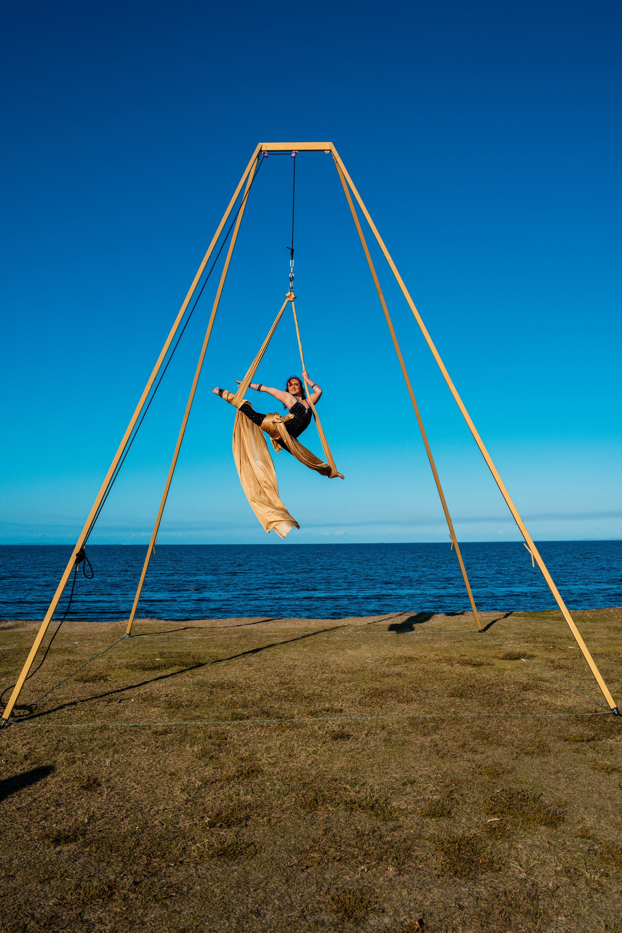 6.4 metre freestanding aerial rig assembled outdoors by the ocean, performer on gold silks