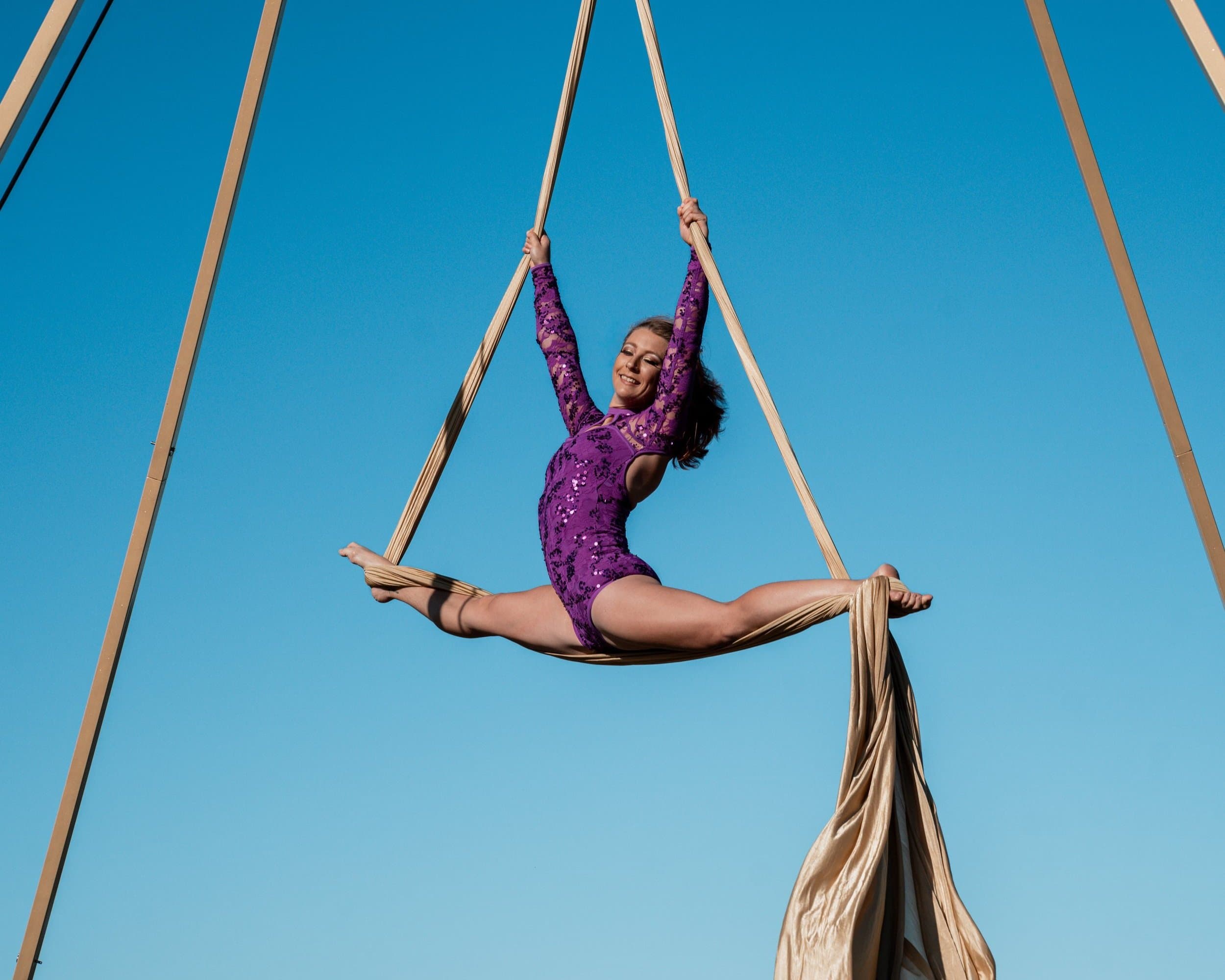Aerialist mid-splits on silks rigged from the hire rig against a blue sky